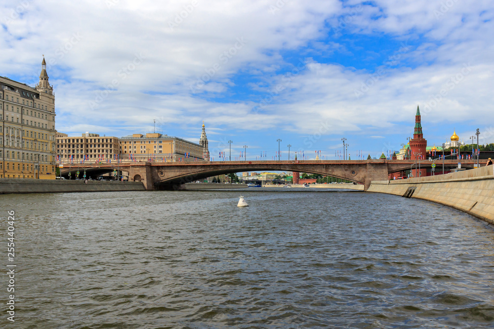 Moskva river surface with stone walls of embankments on a background of Bolshoy Moskvoretskiy Bridge and Moscow Kremlin towers against blue sky at sunny summer morning