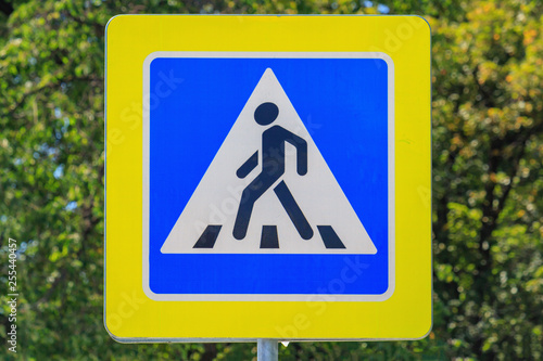 Road sign of Pedestrian crossing against green tree closeup at sunny summer day