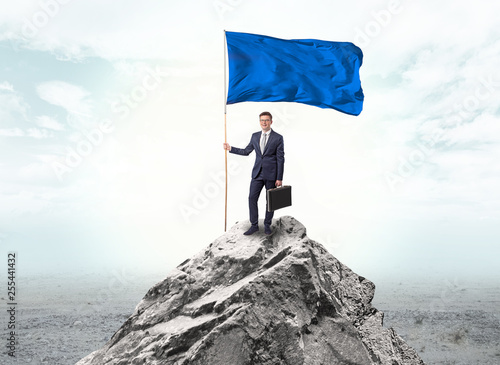 Handsome businessman on the top of the mountain with blue flag 