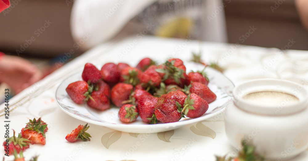 Sweet fresh strawberries on a plate on the table for, hands take and keep ripe red strawberries, a bunch of fresh strawberries in a ceramic bowl on a white table background Sweet fresh strawberries on a plate on the table for, hands take and keep ripe red strawberries, a bunch of fresh strawberries in a ceramic bowl on a white table background