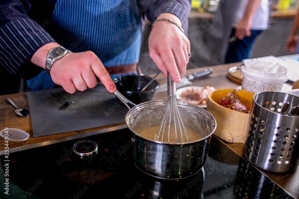 The chef mixes the sauce in a saucepan using the whisk. Master class in the kitchen. The process of cooking. Step by step. Tutorial. Close-up The chef mixes the sauce in a saucepan using the whisk. Master class in the kitchen. The process of cooking. Step by step. Tutorial. Close-up