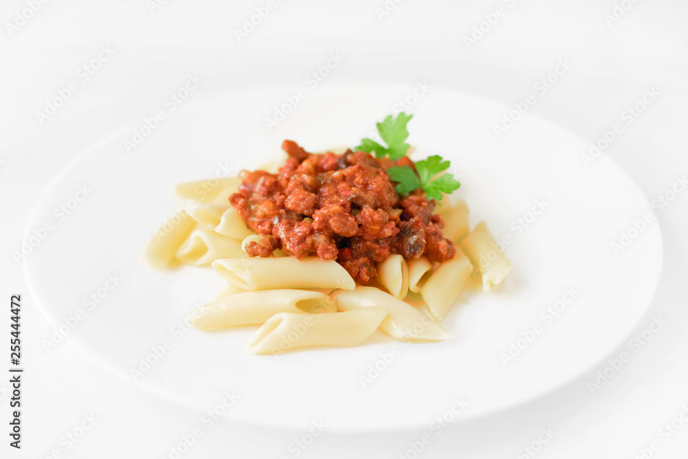 Penne pasta with bolognese sauce and parsley on a white plate, white background Penne pasta with bolognese sauce and parsley on a white plate, white background