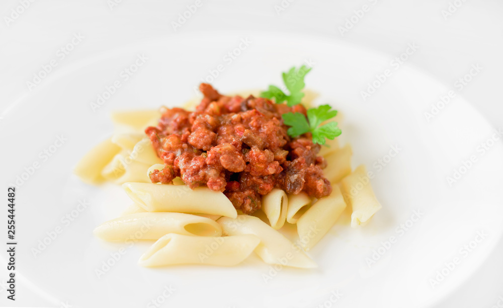 Penne pasta with bolognese sauce and parsley on a white plate, white background, close-up Penne pasta with bolognese sauce and parsley on a white plate, white background, close-up