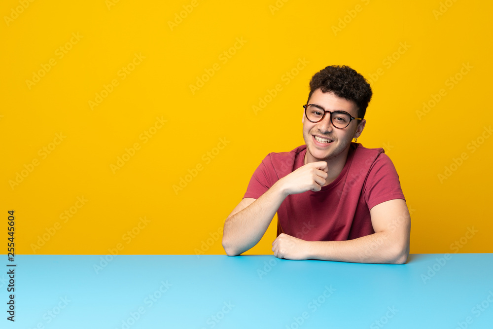 Young man with colorful wall and table with glasses and smiling Young man with colorful wall and table with glasses and smiling