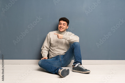 Young man sitting on the floor pointing finger to the side