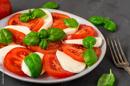 caprese salad with ripe tomatoes and mozzarella cheese, fresh basil leaves on dark concrete background. Italian food