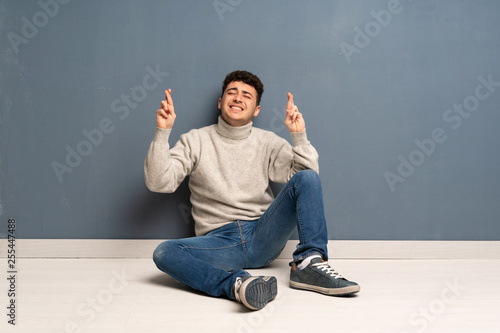 Young man sitting on the floor with fingers crossing and wishing the best