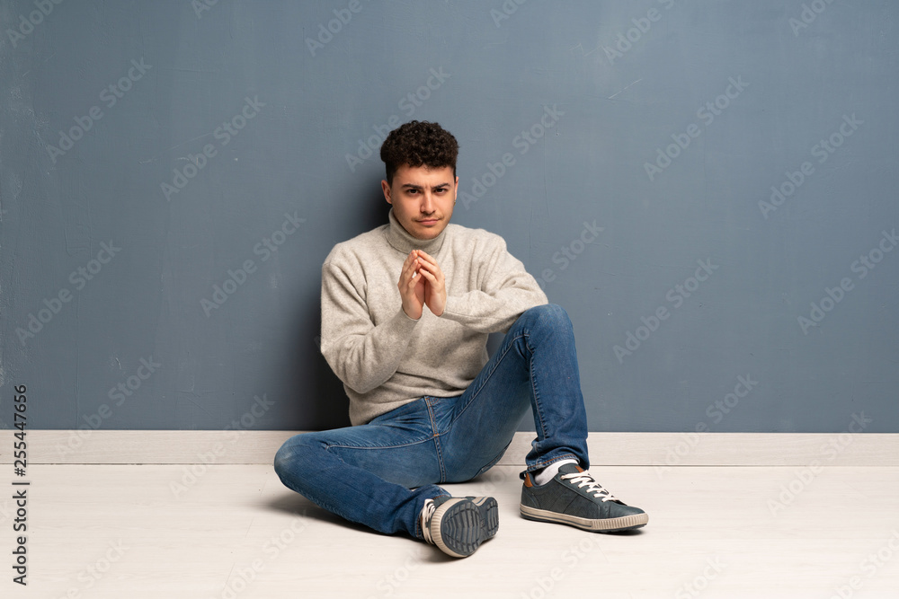 Young man sitting on the floor scheming something Young man sitting on the floor scheming something