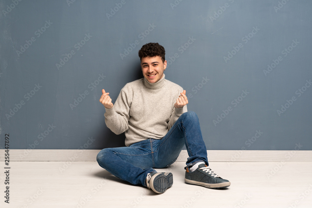 Young man sitting on the floor making money gesture Young man sitting on the floor making money gesture