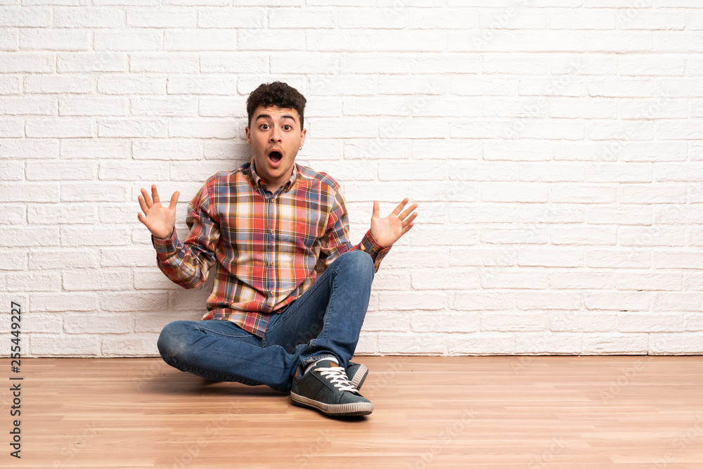 Young man sitting on the floor with shocked facial expression Young man sitting on the floor with shocked facial expression