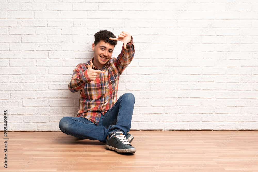 Young man sitting on the floor focusing face. Framing symbol Young man sitting on the floor focusing face. Framing symbol