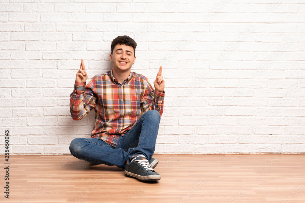 Young man sitting on the floor with fingers crossing and wishing the best Young man sitting on the floor with fingers crossing and wishing the best