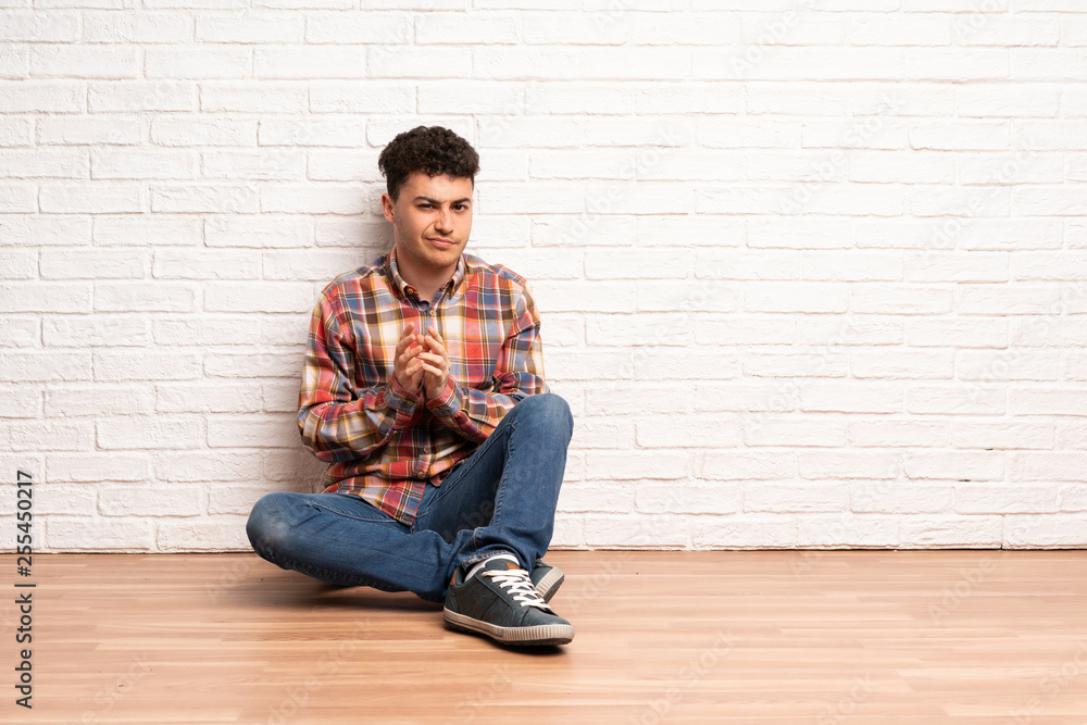 Young man sitting on the floor scheming something Young man sitting on the floor scheming something