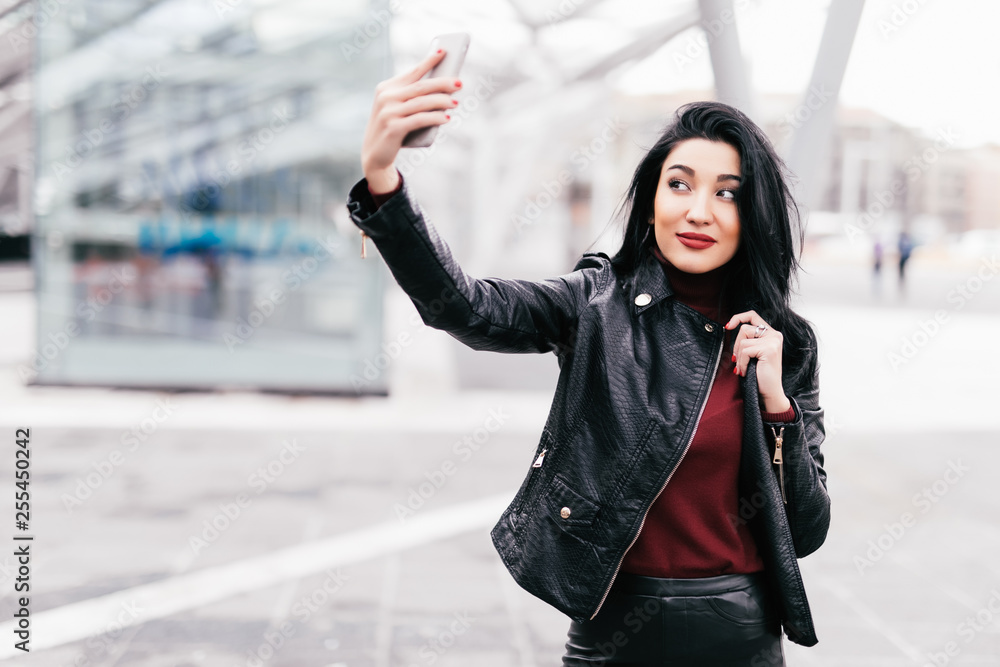 Fototapeta premium Young girl take selfie from hands with phone on autumn city street. Urban life concept.