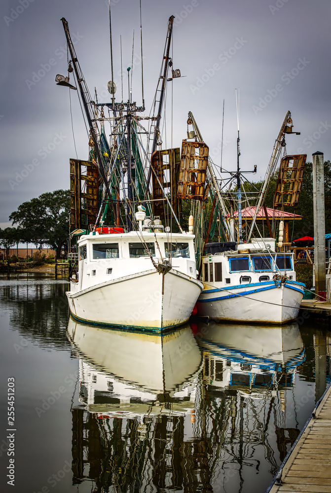 Two shrimp boats docked with reflections in the calm water.