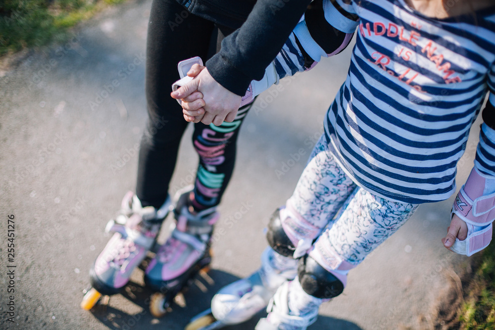 Two young girl standing on roller skates with protection on the knees in park and hold hands