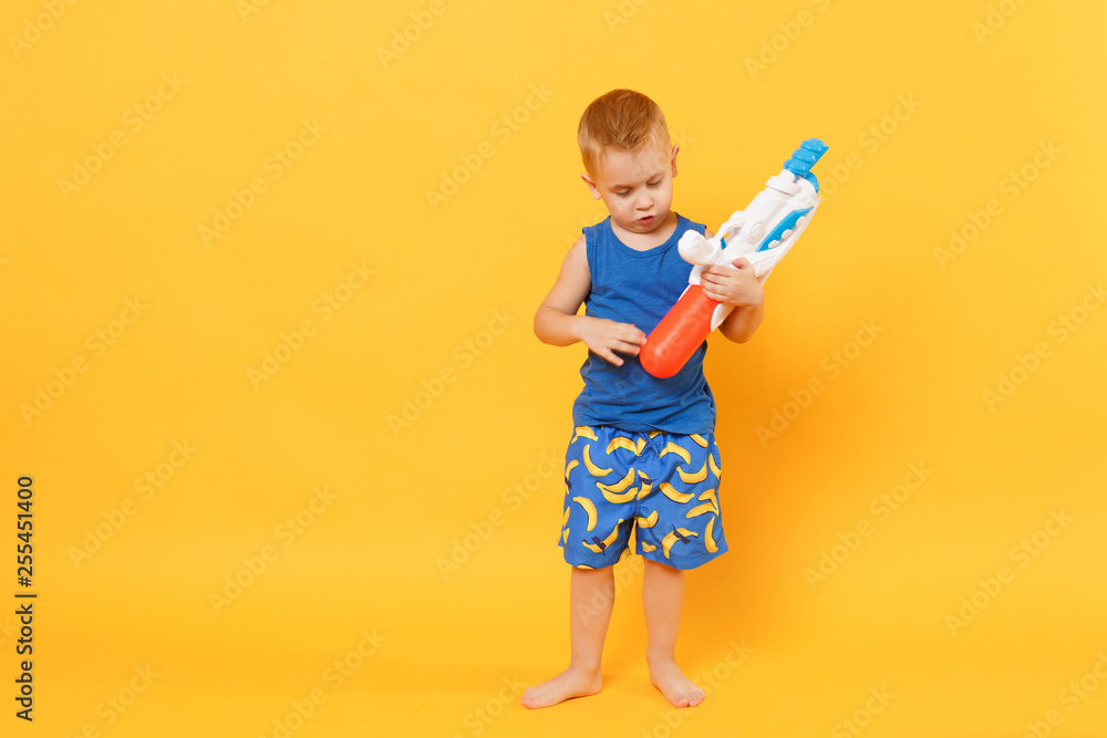 Kid boy 3-4 years old in blue beach summer clothes hold toy water gun isolated on bright yellow orange wall background children studio portrait. People childhood lifestyle concept. Mock up copy space. Kid boy 3-4 years old in blue beach summer clothes hold toy water gun isolated on bright yellow orange wall background children studio portrait. People childhood lifestyle concept. Mock up copy space.