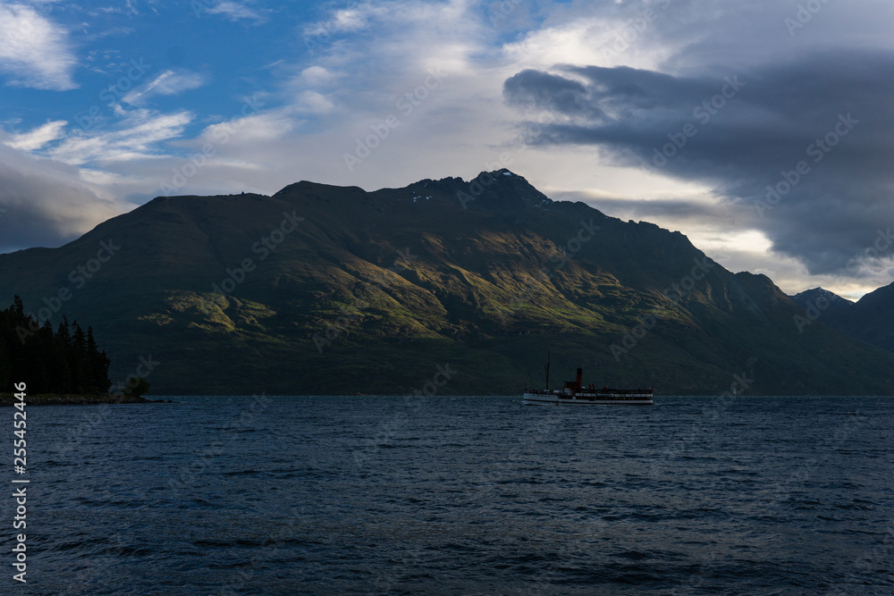 peaceful landscape during sunset with dramatic sky above the lake and mountain range, white ship on the horizon peaceful landscape during sunset with dramatic sky above the lake and mountain range, white ship on the horizon