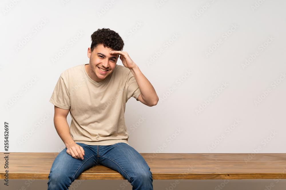 Young man sitting on table looking far away with hand to look something Young man sitting on table looking far away with hand to look something