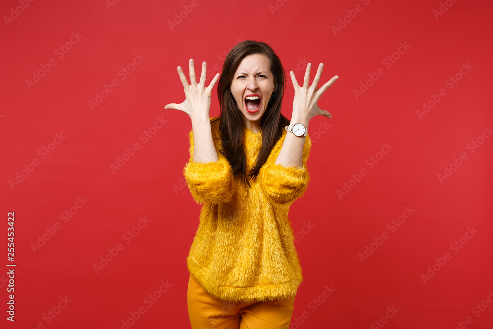 Portrait of angry young woman in yellow fur sweater screaming rising hands spreading fingers isolated on bright red background in studio. People sincere emotions lifestyle concept. Mock up copy space. Portrait of angry young woman in yellow fur sweater screaming rising hands spreading fingers isolated on bright red background in studio. People sincere emotions lifestyle concept. Mock up copy space.
