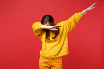 Portrait of young woman in yellow fur sweater with lowered head showing dab dance gesture isolated on bright red background in studio. People sincere emotions, lifestyle concept. Mock up copy space.