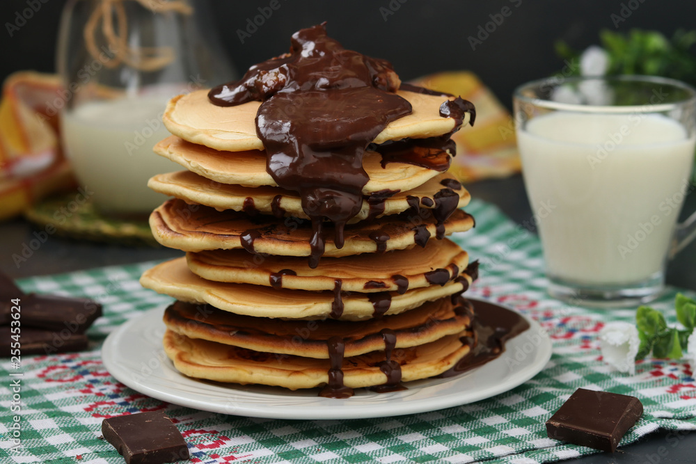 Pancakes with bananas on a plate against a dark background, behind is a jug and a glass of milk Pancakes with bananas on a plate against a dark background, behind is a jug and a glass of milk
