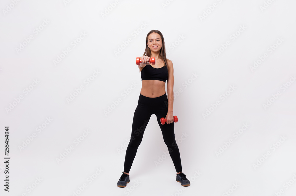 Beautiful woman in black sportwear doing exercises with dumbells over white background