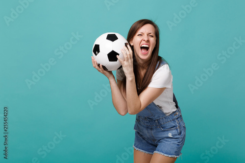 Crazy screaming woman football fan cheer up support favorite team with soccer ball isolated on blue turquoise background. People emotions, sport family leisure lifestyle concept. Mock up copy space. © ViDi Studio