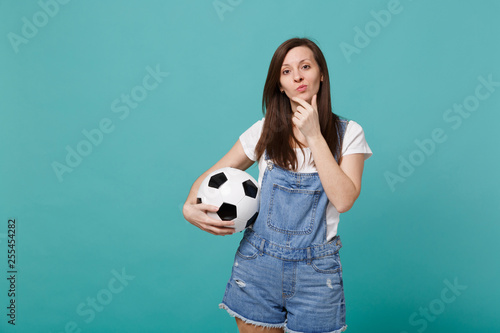 Pensive woman football fan support favorite team with soccer ball put hand prop up on chin isolated on blue turquoise wall background. People emotions sport family leisure concept. Mock up copy space. © ViDi Studio