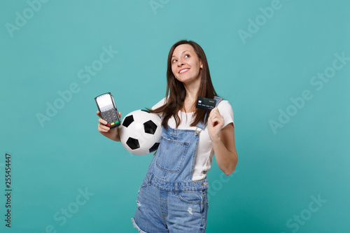 Dreamful woman football fan looking up, support favorite team with soccer ball, wireless modern bank payment terminal to process and acquire credit card payments isolated on blue turquoise background. © ViDi Studio
