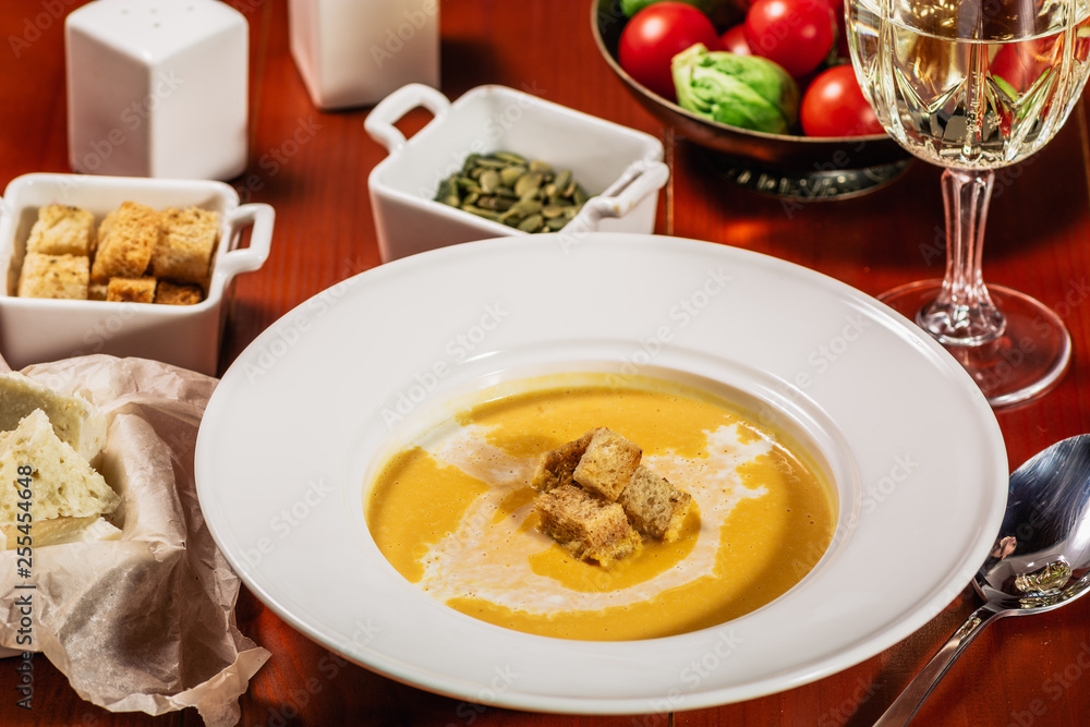 Roasted pumpkin and carrot soup with cream, pumpkin seeds. Served with croutons, cheese and white wine on wooden background. Copy space Roasted pumpkin and carrot soup with cream, pumpkin seeds. Served with croutons, cheese and white wine on wooden background. Copy space