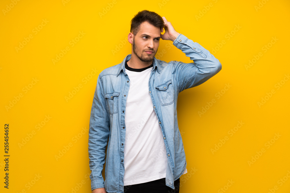 Handsome man over yellow wall having doubts while scratching head Handsome man over yellow wall having doubts while scratching head