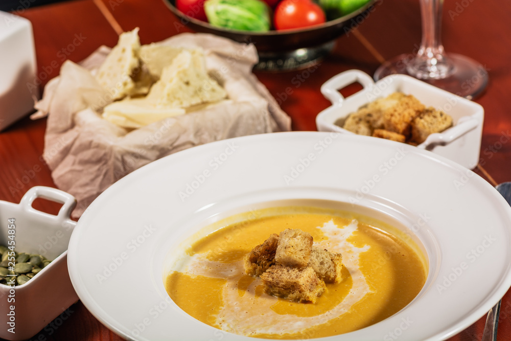 Pumpkin cream soup with croutons, baked chickpeas, sesame, parsley on a brown wooden background. Baked chickpeas with spices. Useful dietary snacks. Served with white wine and cheese Pumpkin cream soup with croutons, baked chickpeas, sesame, parsley on a brown wooden background. Baked chickpeas with spices. Useful dietary snacks. Served with white wine and cheese