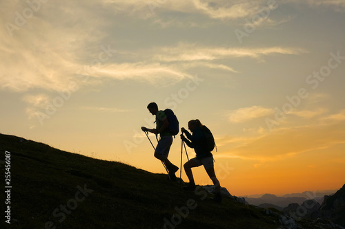 SILHOUETTE: Cheerful tourist couple are trekking up a grassy hill at sunset.