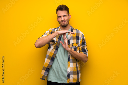 Handsome man over yellow wall making time out gesture