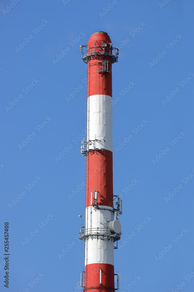 High chimney at the plant in red-white color with equipment for broadcasting radio. Installing a cellular antenna. Combining the use of factory chimneys and high technology