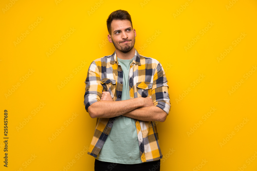 Handsome man over yellow wall making doubts gesture while lifting the shoulders Handsome man over yellow wall making doubts gesture while lifting the shoulders