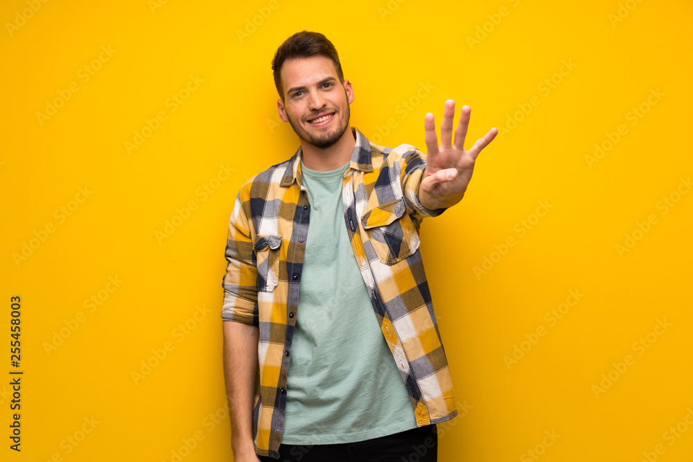 Handsome man over yellow wall happy and counting four with fingers Handsome man over yellow wall happy and counting four with fingers