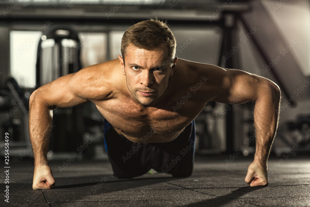 Obraz premium No way back. Handsome young serious motivated fitness man looking to the camera confidently doing pushups at the gym workout muscular power strength endurance energy sport health challenge concept