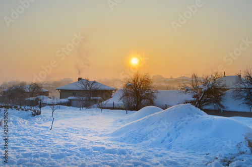 Winter Rural Landscape - Mountain Village Covered with Snow .Misty Morning with Orange Sunrise Sky.