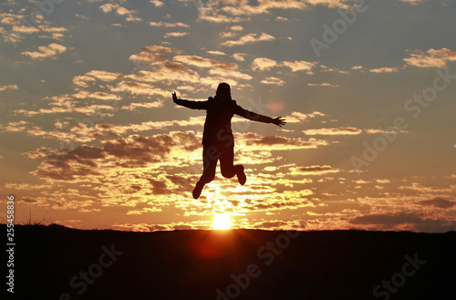 Silhouette of a happy girl jumping into the sky against the backdrop of an incredible sunset  sky and clouds