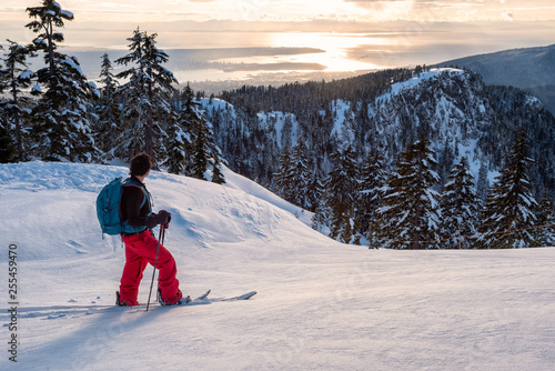 Adventurous man is backcountry skiing up Mount Seymour during a sunny winter sunset. Taken in North Vancouver, BC, Canada. photo