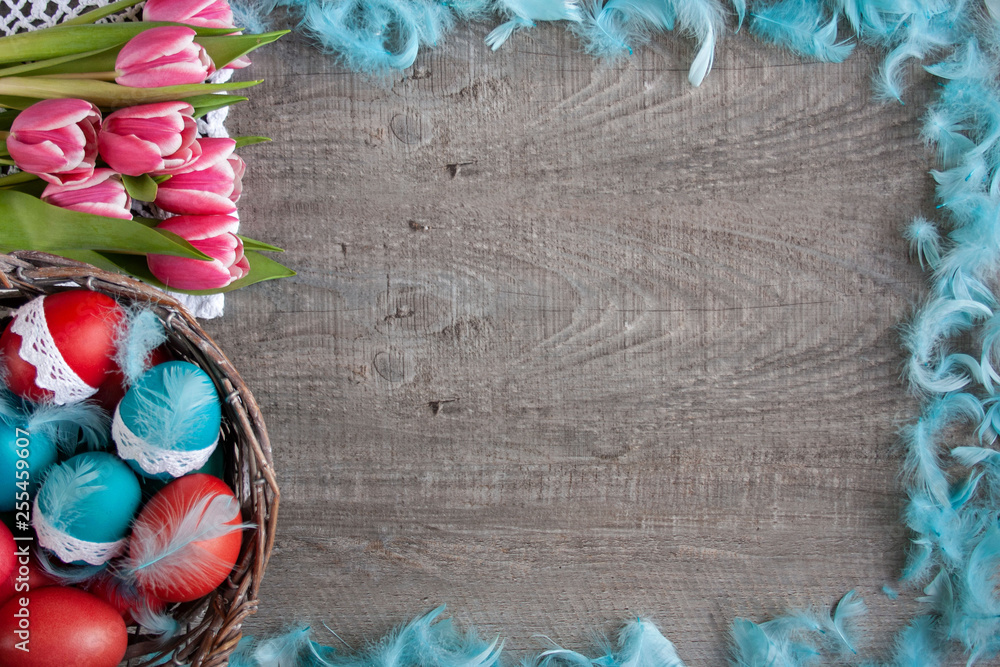 Wielkanocne tło z różowymi tulipanami, koszykiemi pełnym pisanek i niebieskimi piórami - obrazy, fototapety, plakaty 