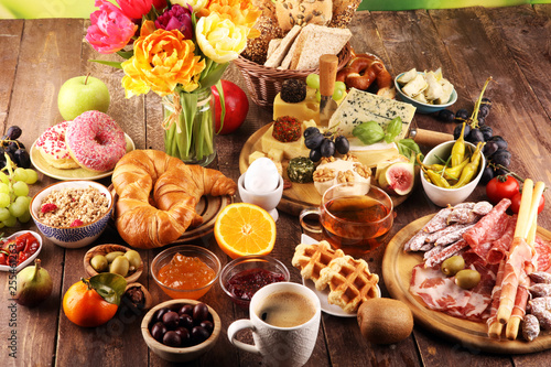 breakfast on table with bread buns, croissants, coffe and eggs