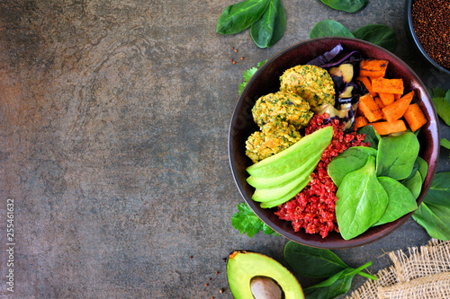 Healthy vegan buddha bowl with falafels, beet quinoa, avocado, and vegetables on a dark stone background. Healthy eating concept. Side border with copy space.
