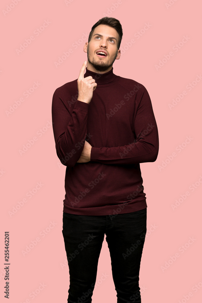 Man with turtleneck sweater pointing with the index finger a great idea over pink background Man with turtleneck sweater pointing with the index finger a great idea over pink background