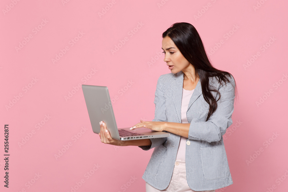 Portrait of attractive brunette young woman in striped jacket using laptop pc computer isolated on pink pastel wall background in studio. People sincere emotions lifestyle concept. Mock up copy space. Portrait of attractive brunette young woman in striped jacket using laptop pc computer isolated on pink pastel wall background in studio. People sincere emotions lifestyle concept. Mock up copy space.