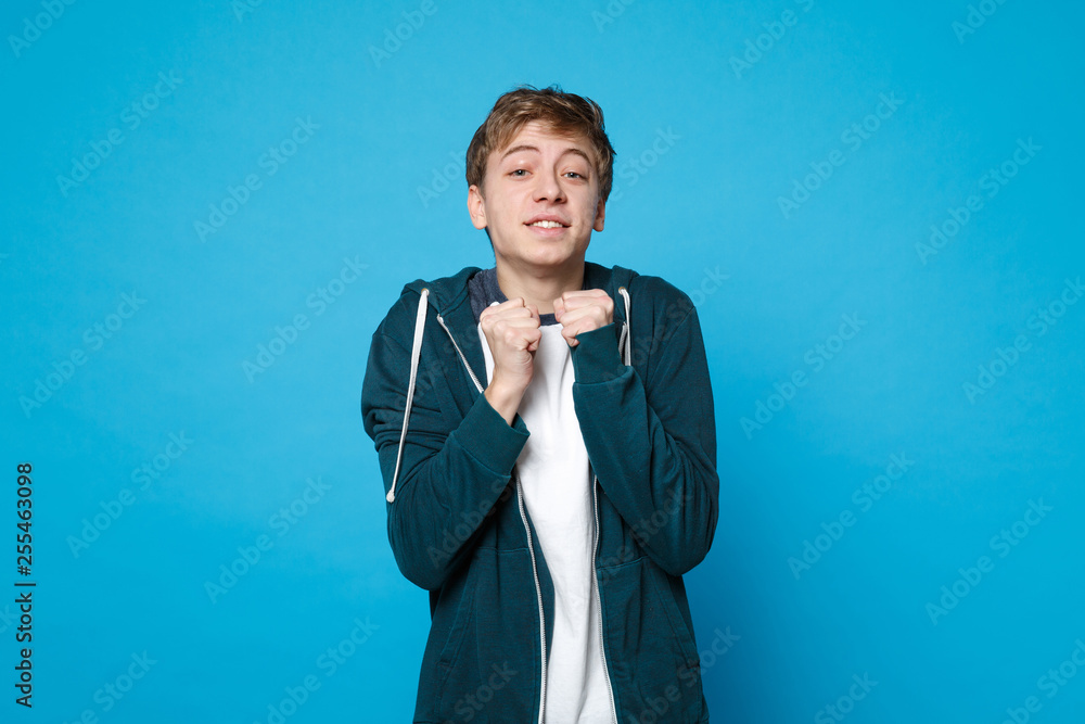 Portrait of waiting pleading young man in casual clothes standing and clenching fists isolated on blue wall background in studio. People sincere emotions, lifestyle concept. Mock up copy space. Portrait of waiting pleading young man in casual clothes standing and clenching fists isolated on blue wall background in studio. People sincere emotions, lifestyle concept. Mock up copy space.