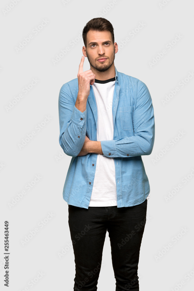 Handsome man thinking an idea pointing the finger up over grey background