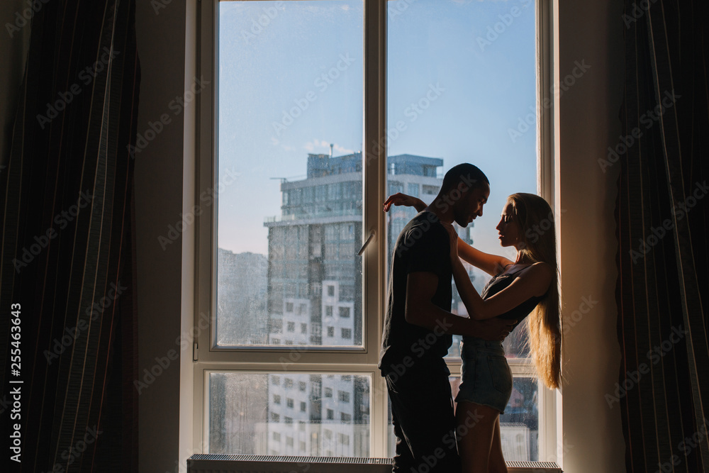 Lovely sweet moments of cute copule hugging near window in the morning in modern apartment. Being in love, hugging, relationship, home, cheerful mood, true emotions